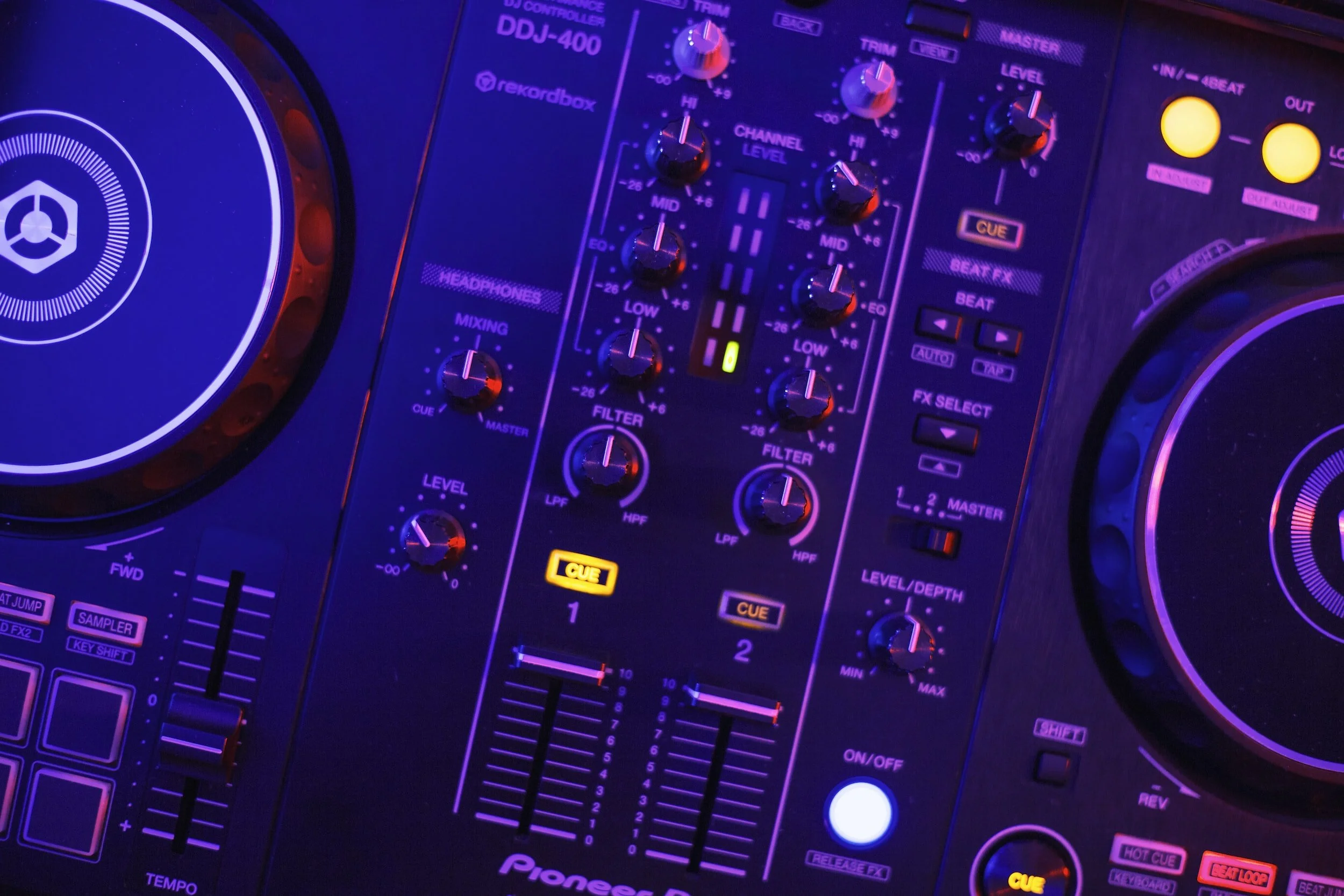 Close-up of a DJ controller’s mixer and jog wheels under purple light