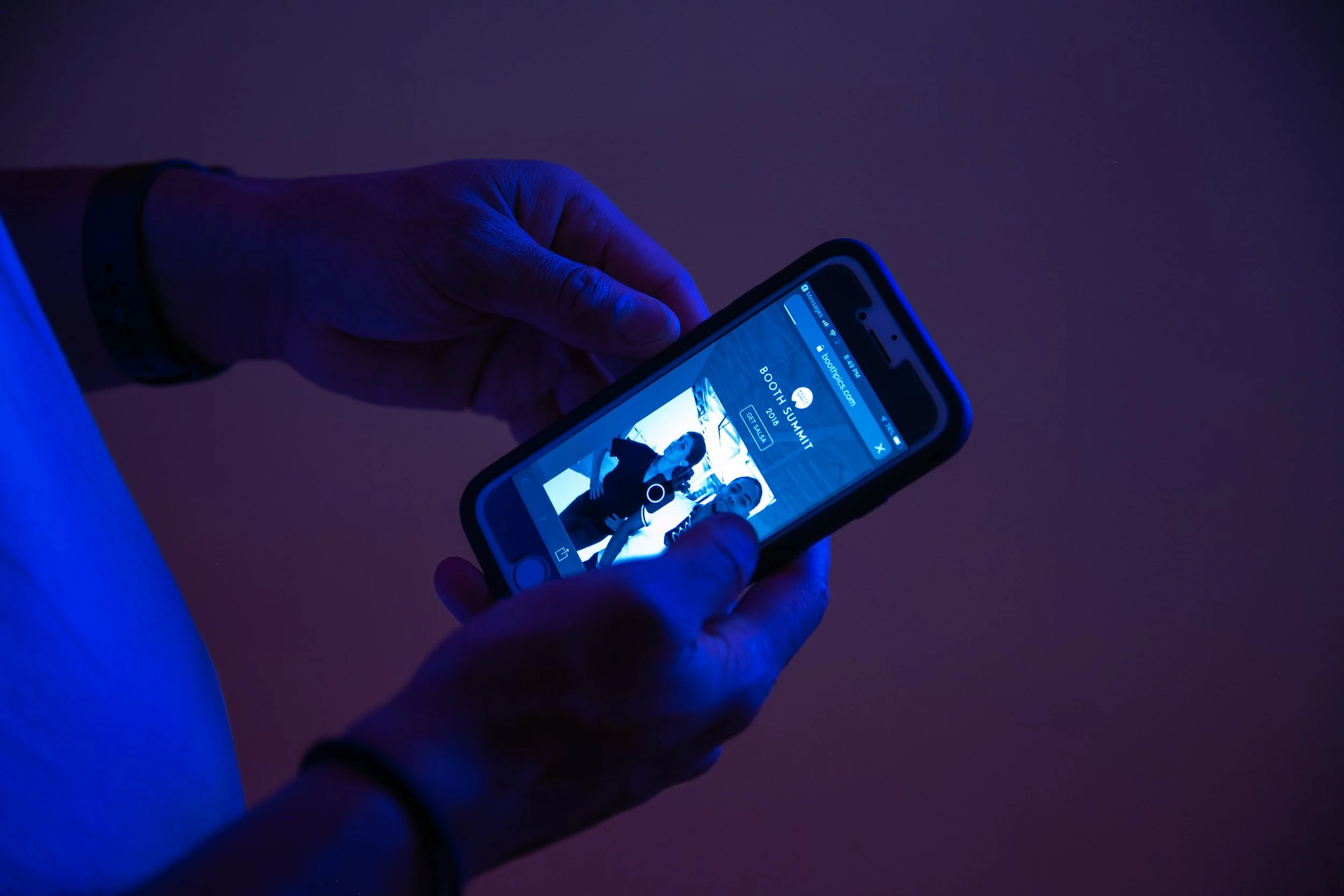 Hands holding a phone showing a photo booth picture under blue light