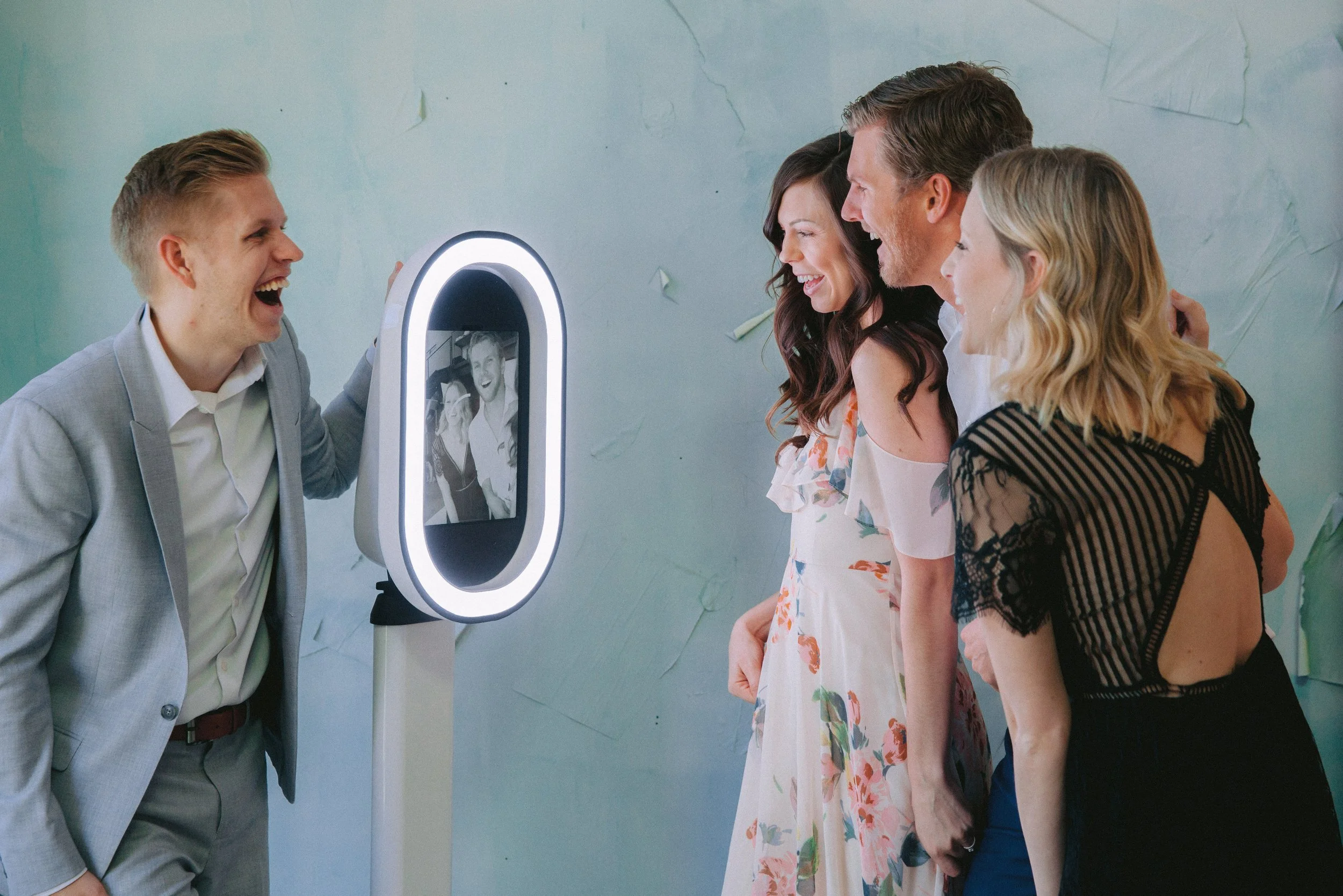 Four friends laughing at the photo booth and its glowing ring-light screen