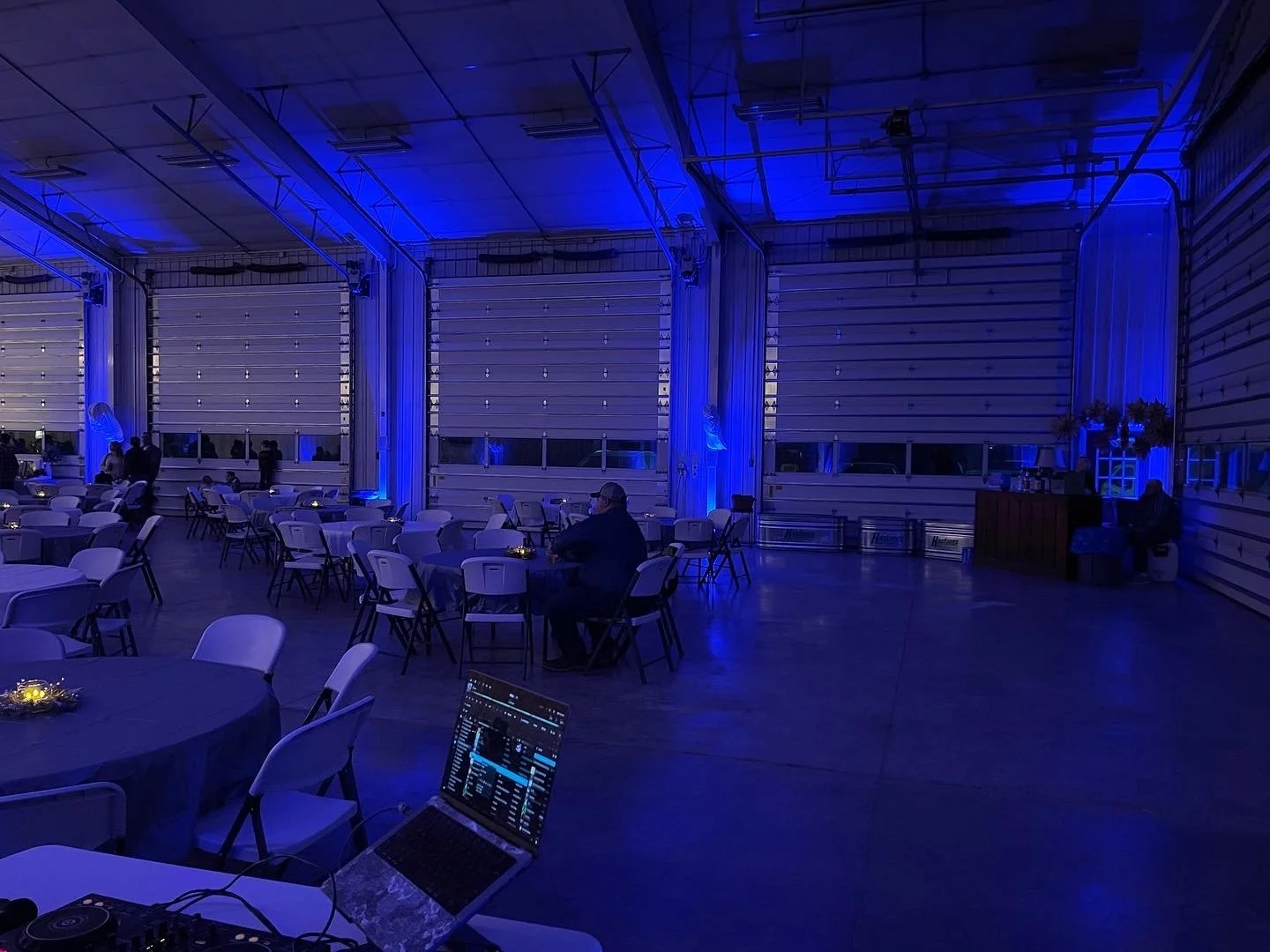 Blue uplighting in a venue with tall ceilings, concrete floors and large garage doors.
